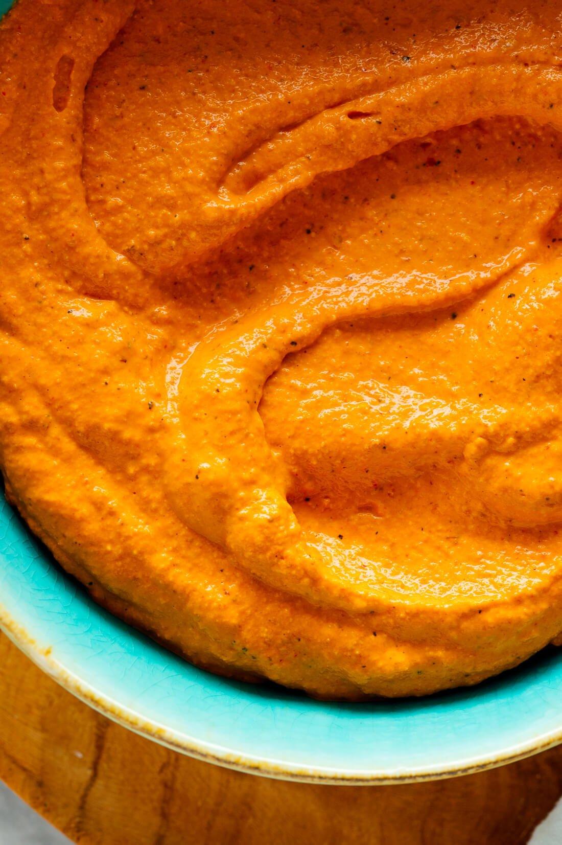 Close-up shot of the romesco sauce being poured over the stuffed peppers