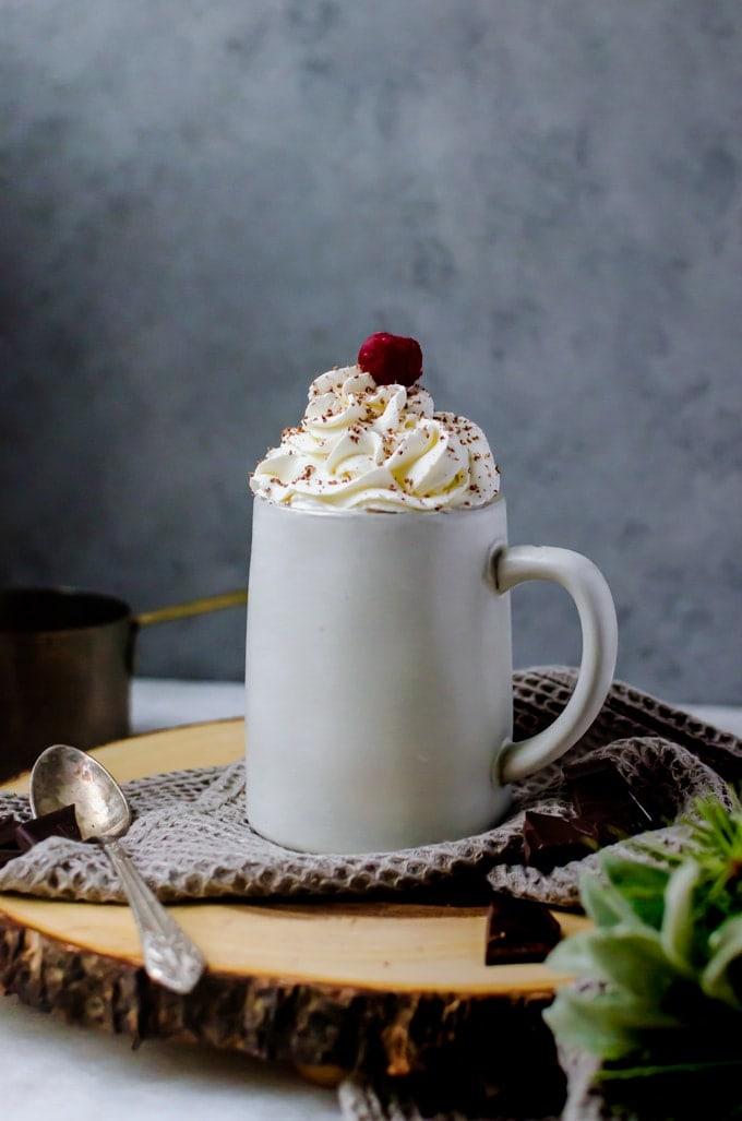 Close-up shot of a mug of Black Forest Hot Chocolate garnished with chocolate shavings and a cherry
