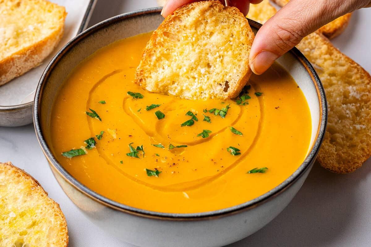 Warm roasted carrot soup with fresh thyme, rosemary, and crusty bread, cozy winter kitchen scene