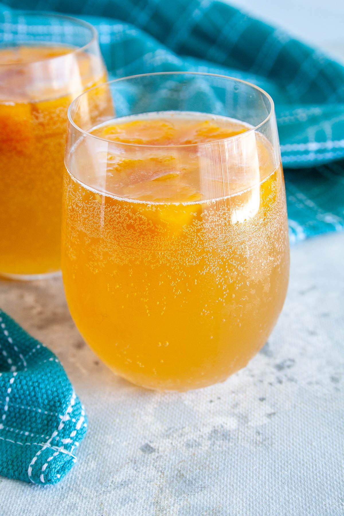 Close-up of a glass bottle filled with bubbly peach kombucha, with fresh peaches in the background