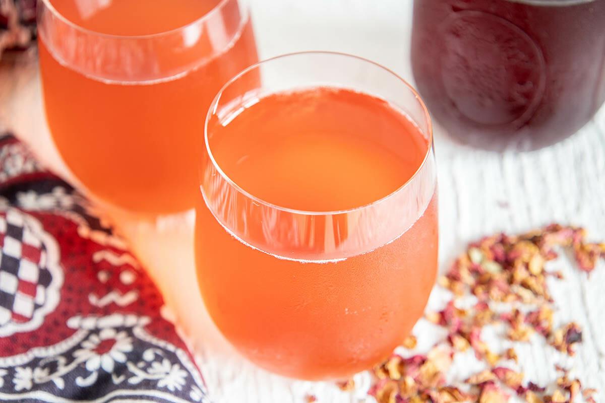 Close-up of a glass bottle of apricot kombucha with rosewater, garnished with fresh apricots and rose petals