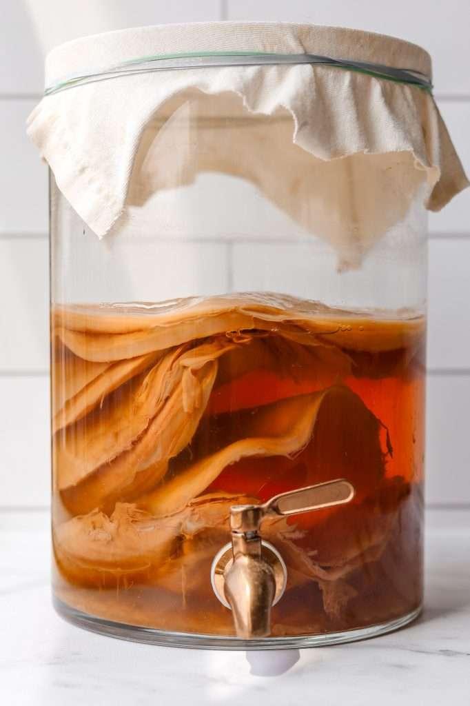 A closeup of a dark amber kombucha vinegar in a clear glass bottle with some kombucha tea leaves
