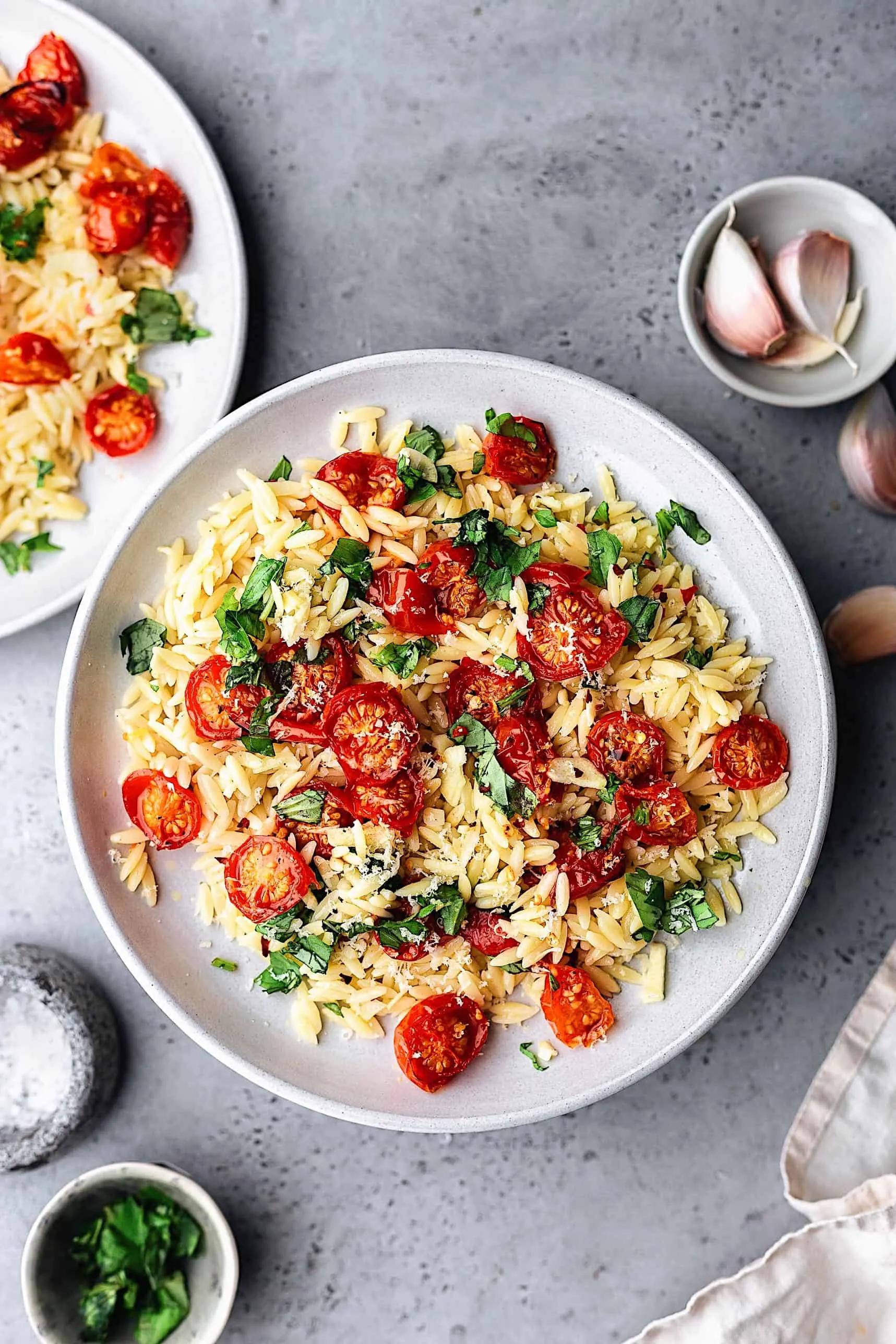 Close up shot of a bowl of Garlic Parmesan Orzo with Burst Cherry Tomatoes, garnished with fresh parsley.