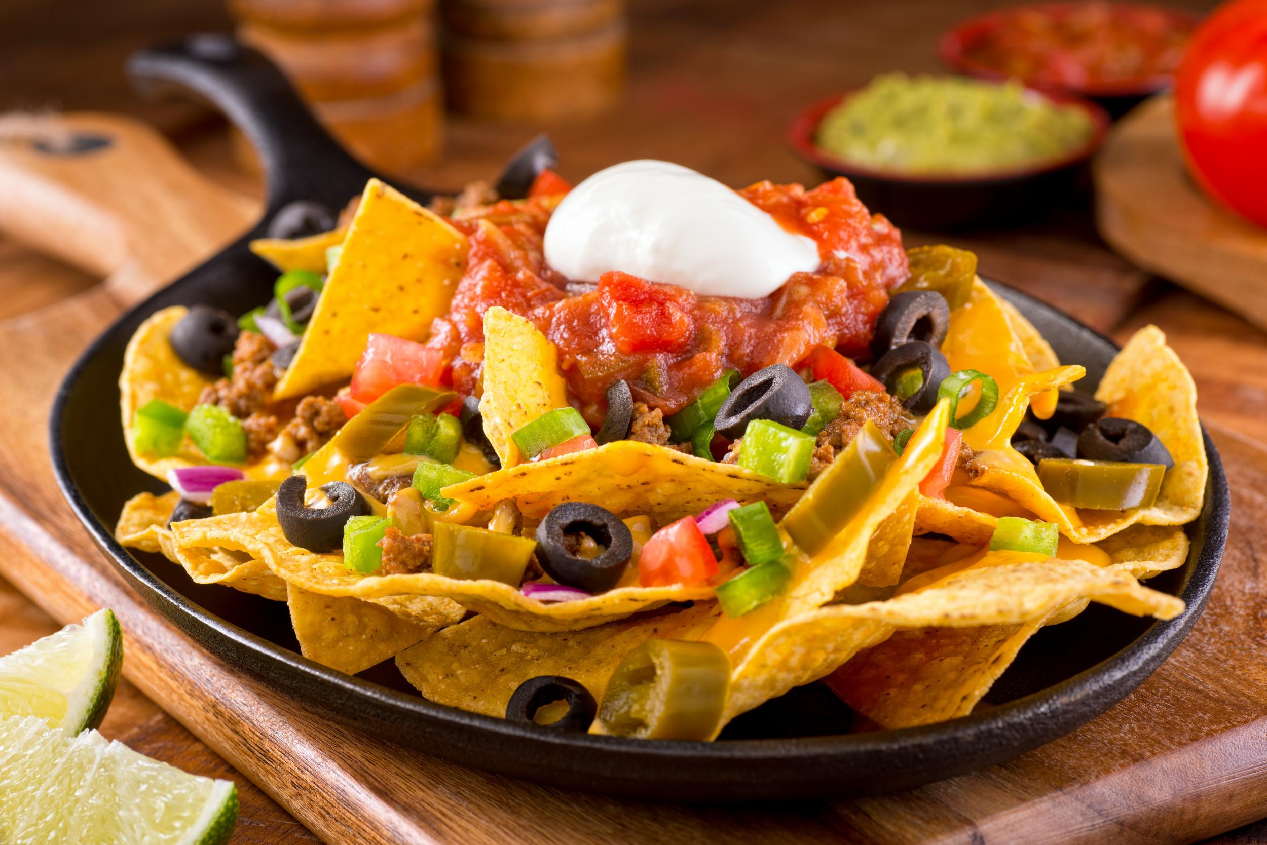 A plate of nachos with melted burrata cheese, various toppings, and tortilla chips