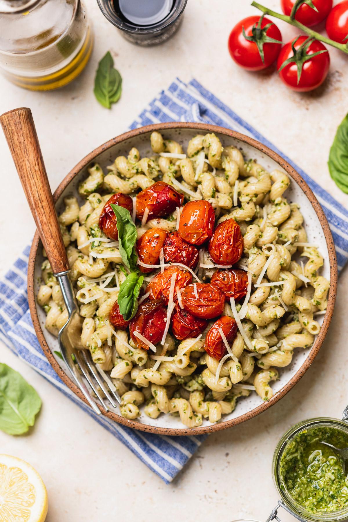 Cilantro pesto pasta with roasted cherry tomatoes being tossed in a bowl