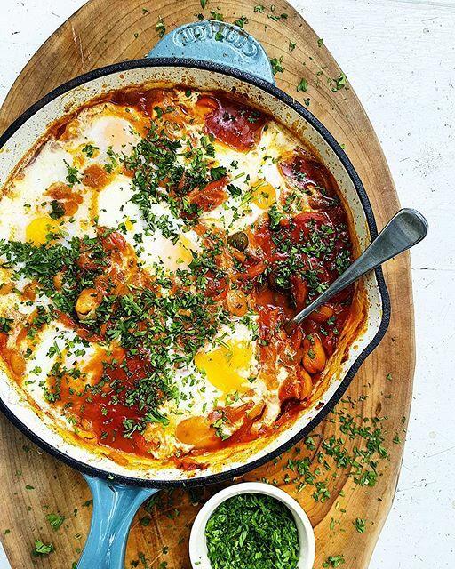 Overhead shot of shakshuka with lobster and truffle oil in a rustic skillet, garnished with fresh herbs