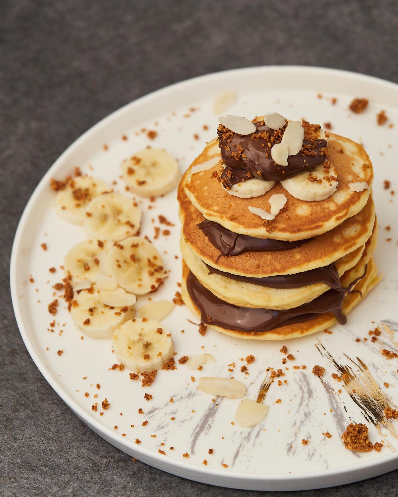Person smiling while eating banana pancakes with Nutella