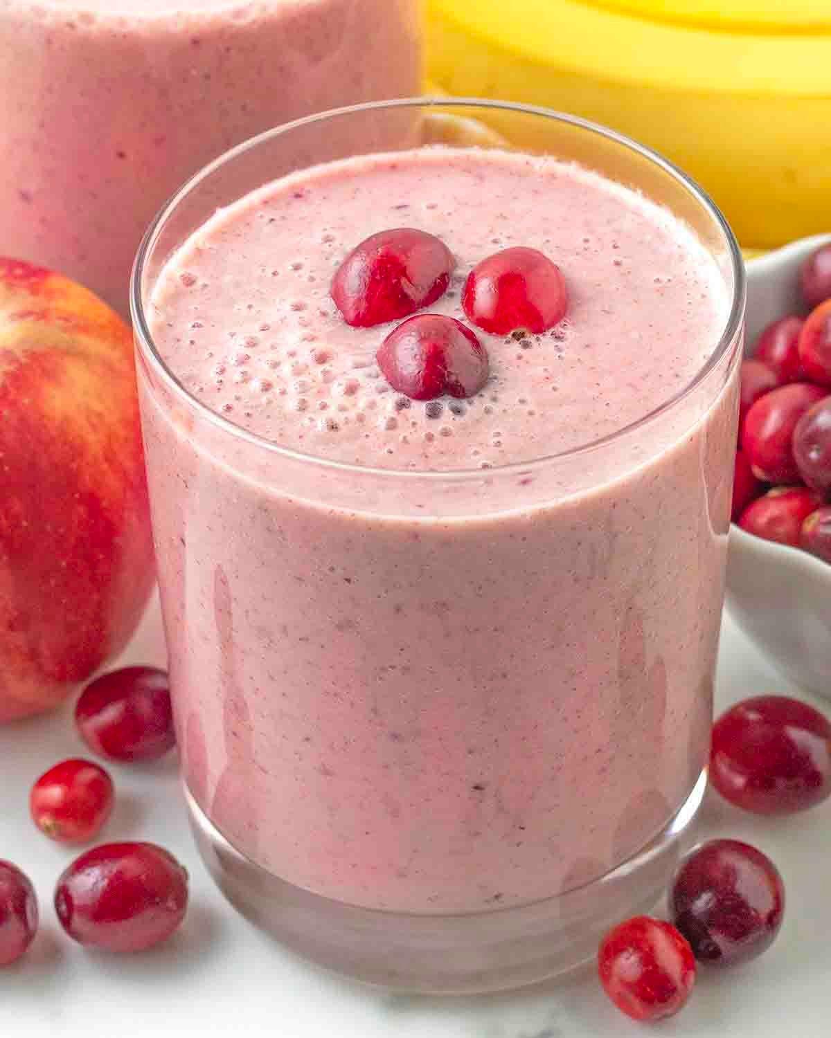 Close-up shot of a vibrant cranberry apple crisp smoothie in a glass with cranberries and apple slices garnishing the rim