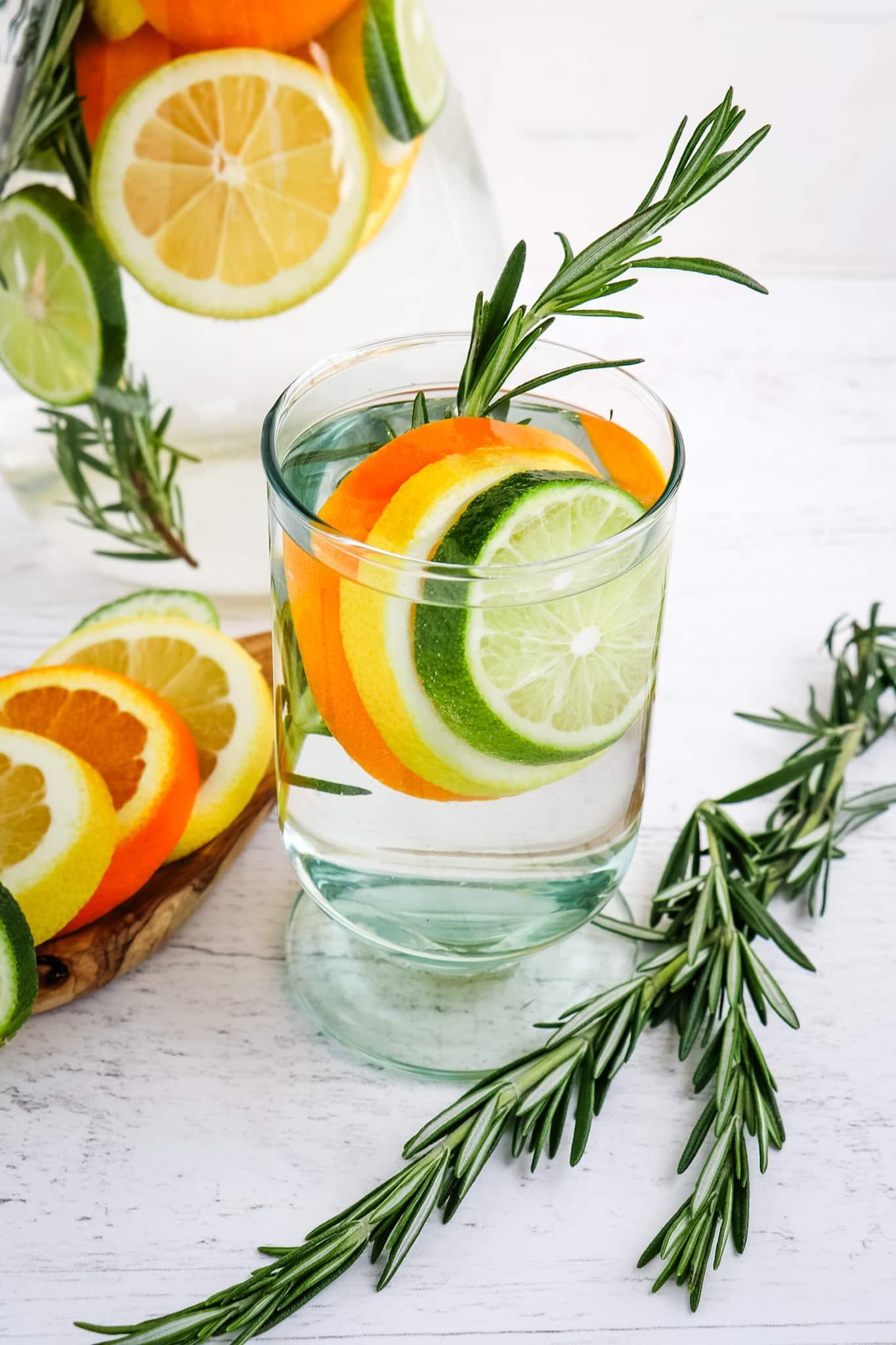 A close-up shot of a glass of rosemary-citrus infused water with ice cubes and a rosemary sprig