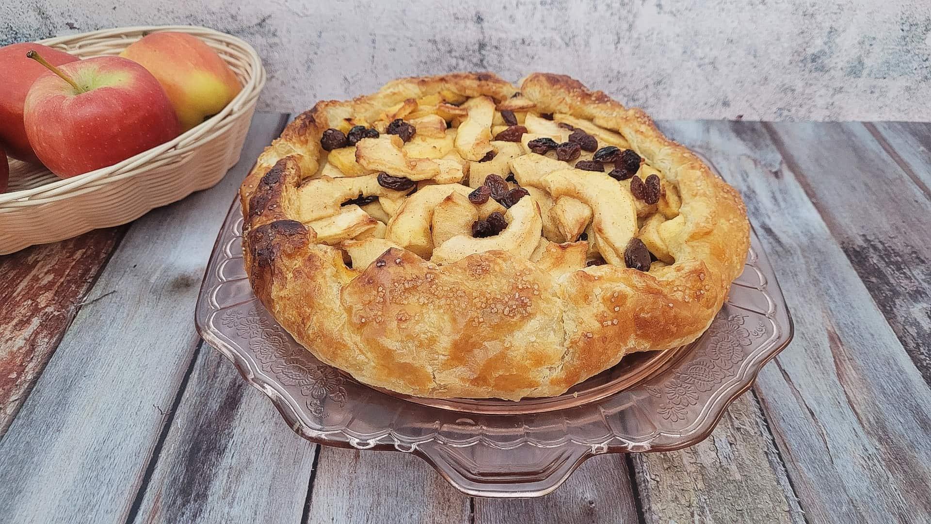 A rustic apple pie with a pretzel crust, apples peeking out from the edges, sitting on a wooden table
