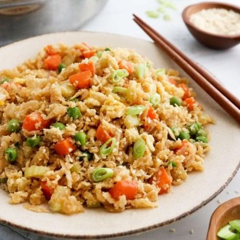 A wide shot of a table with several plates of cauliflower fried rice, surrounded by friends and family