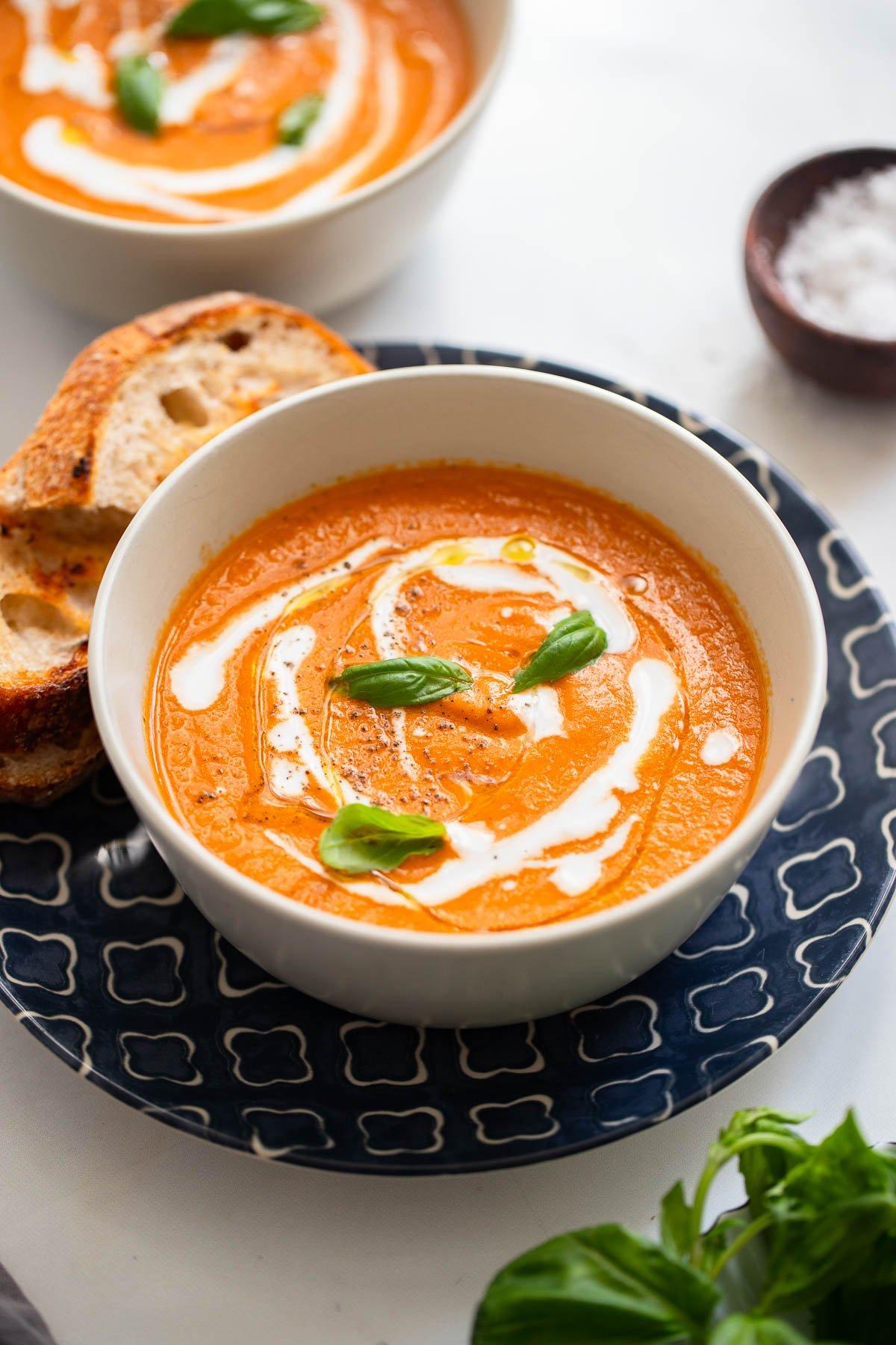 A bowl of creamy vegan tomato soup with roasted red peppers, garnished with fresh basil