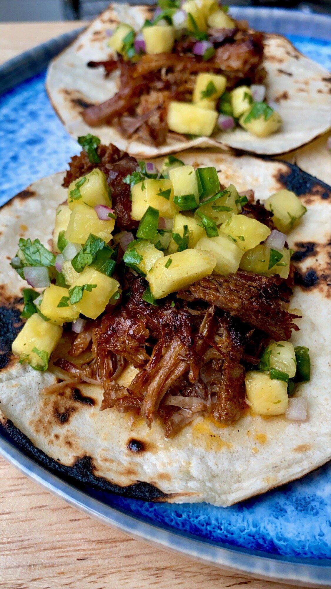 Kimchi carnitas tacos with pineapple salsa on a rustic wooden table