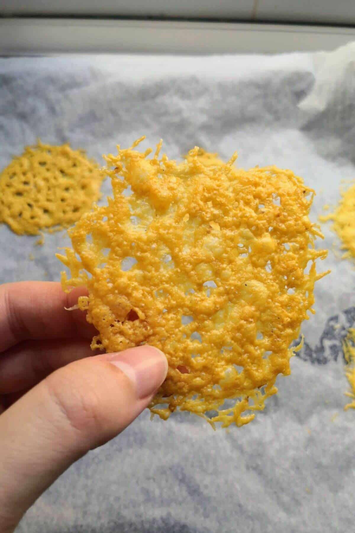 A person holding a baking sheet of coconut flour parmesan crisps