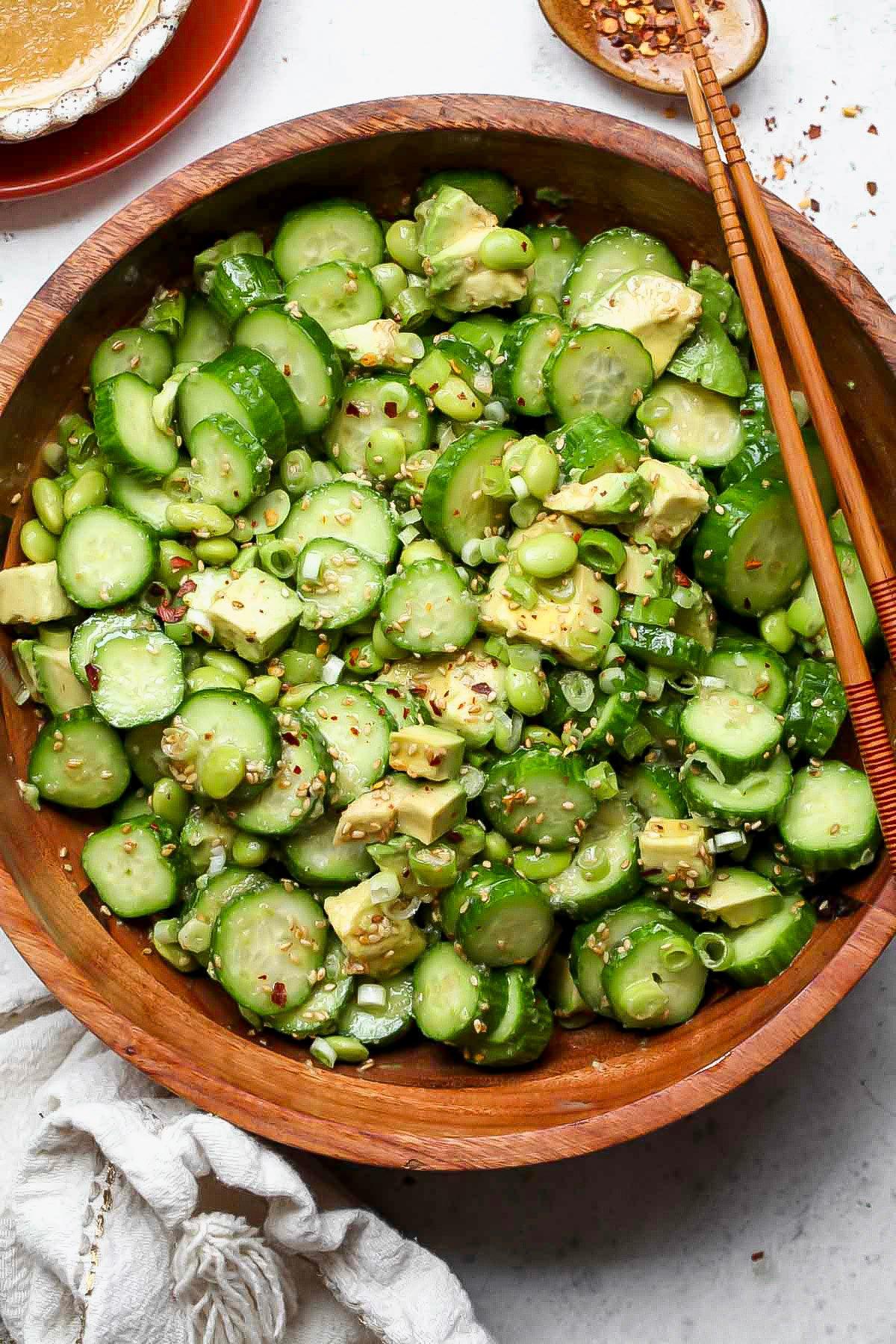 A hand pouring sesame ginger dressing over the edamame salad in a mixing bowl