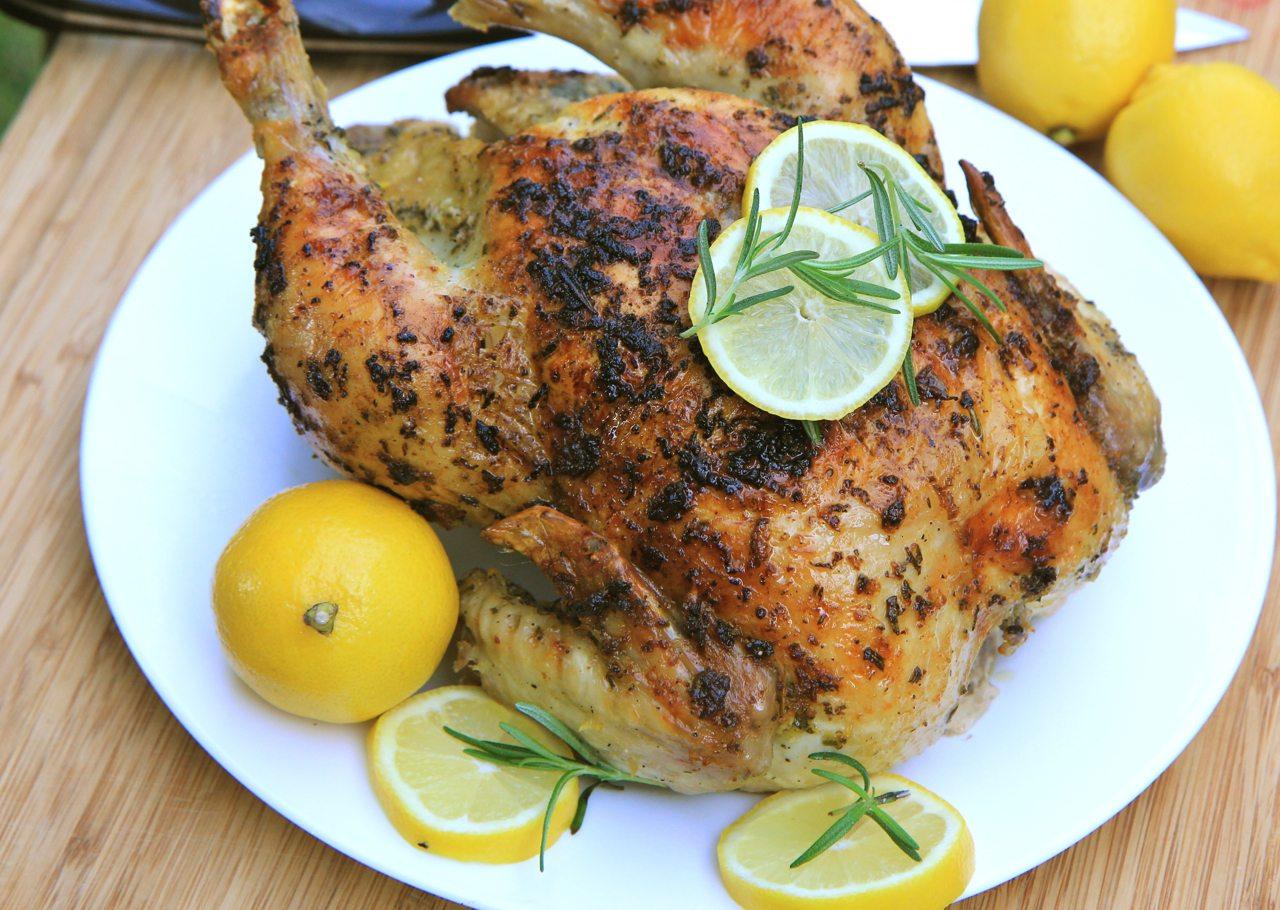 A juicy rosemary roasted chicken with lemon and garlic, glistening and golden brown, served on a rustic wooden platter.