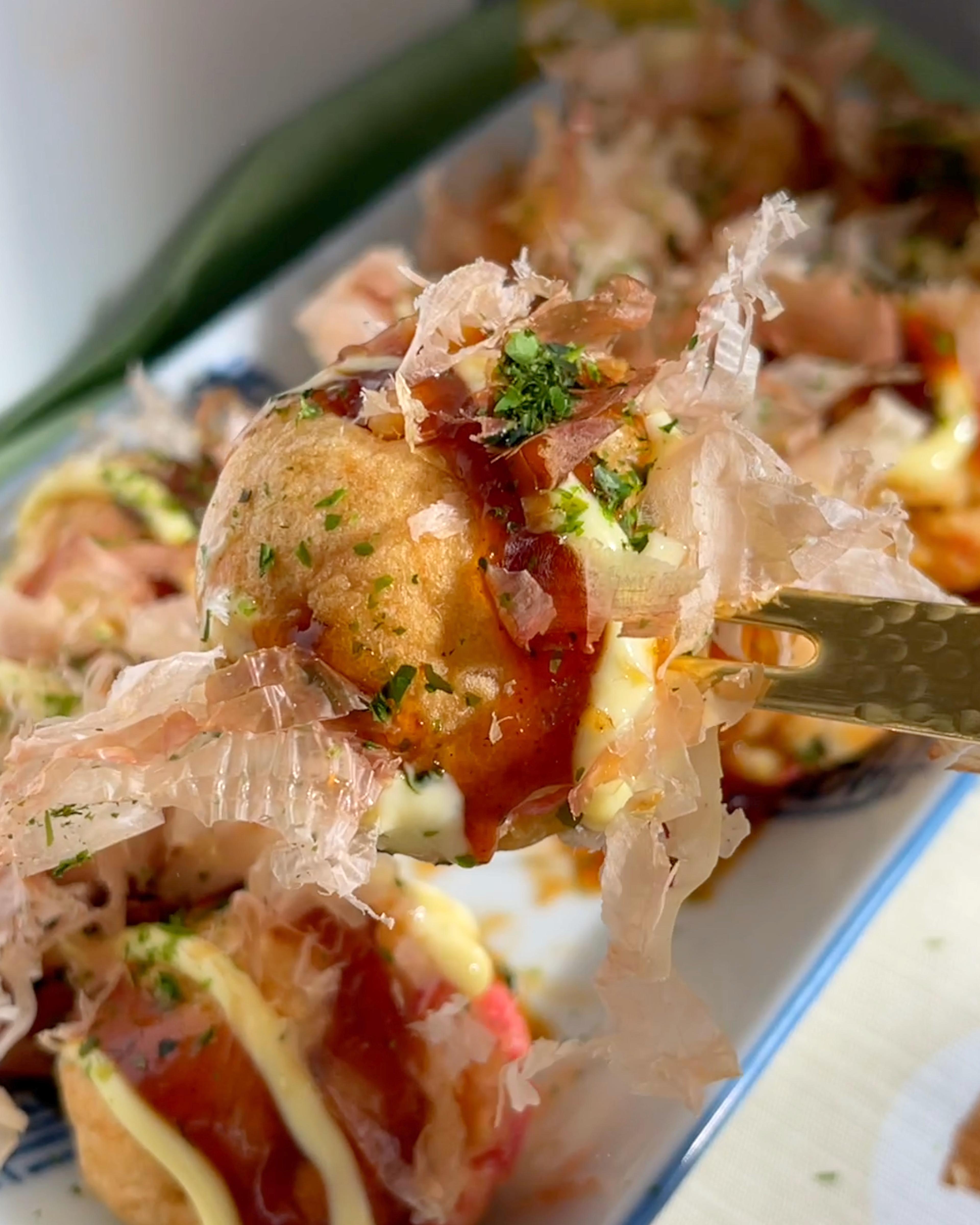 Close-up shot of golden brown takoyaki balls drizzled with Massaman curry sauce, garnished with chopped peanuts and cilantro