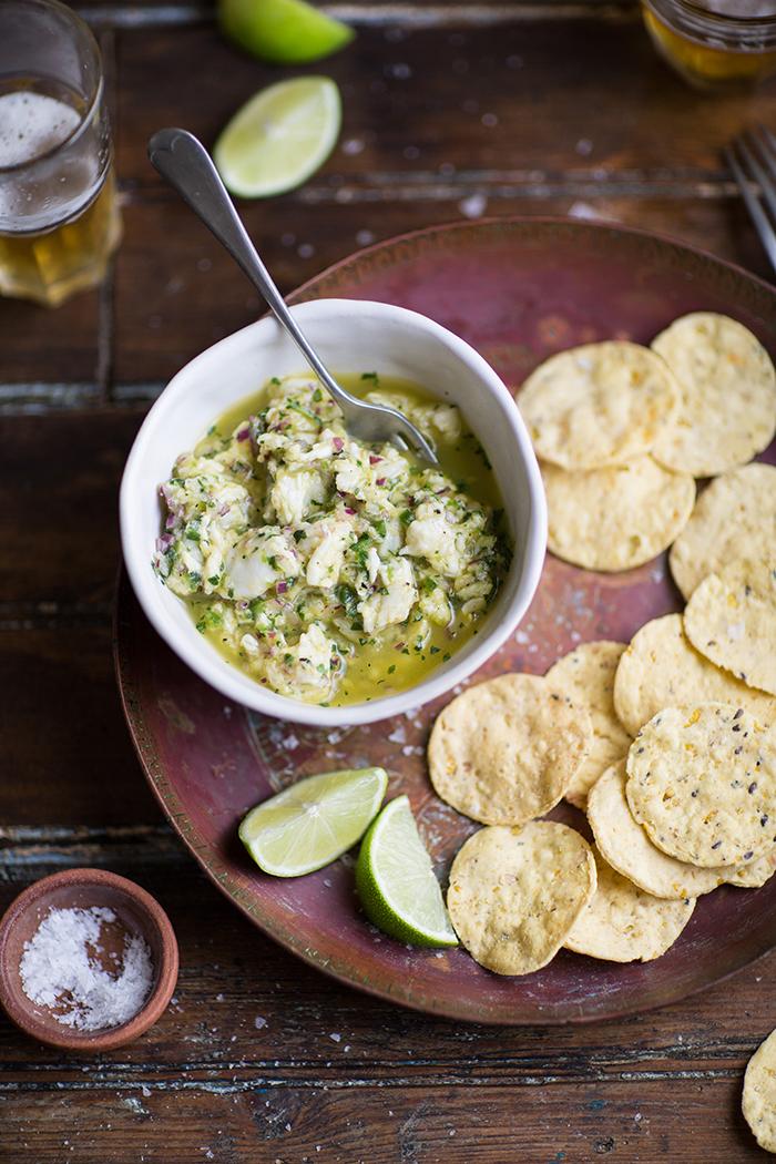 A bowl of ceviche with aji amarillo paste, garnished with cilantro and lime wedges