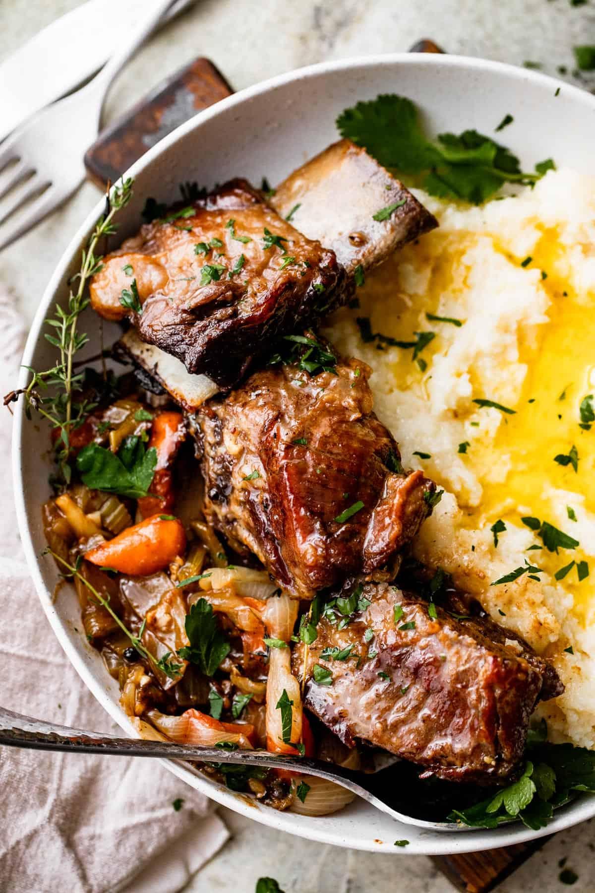 A rustic wooden table set with a bowl of slow-cooked beef short ribs and mashed potatoes