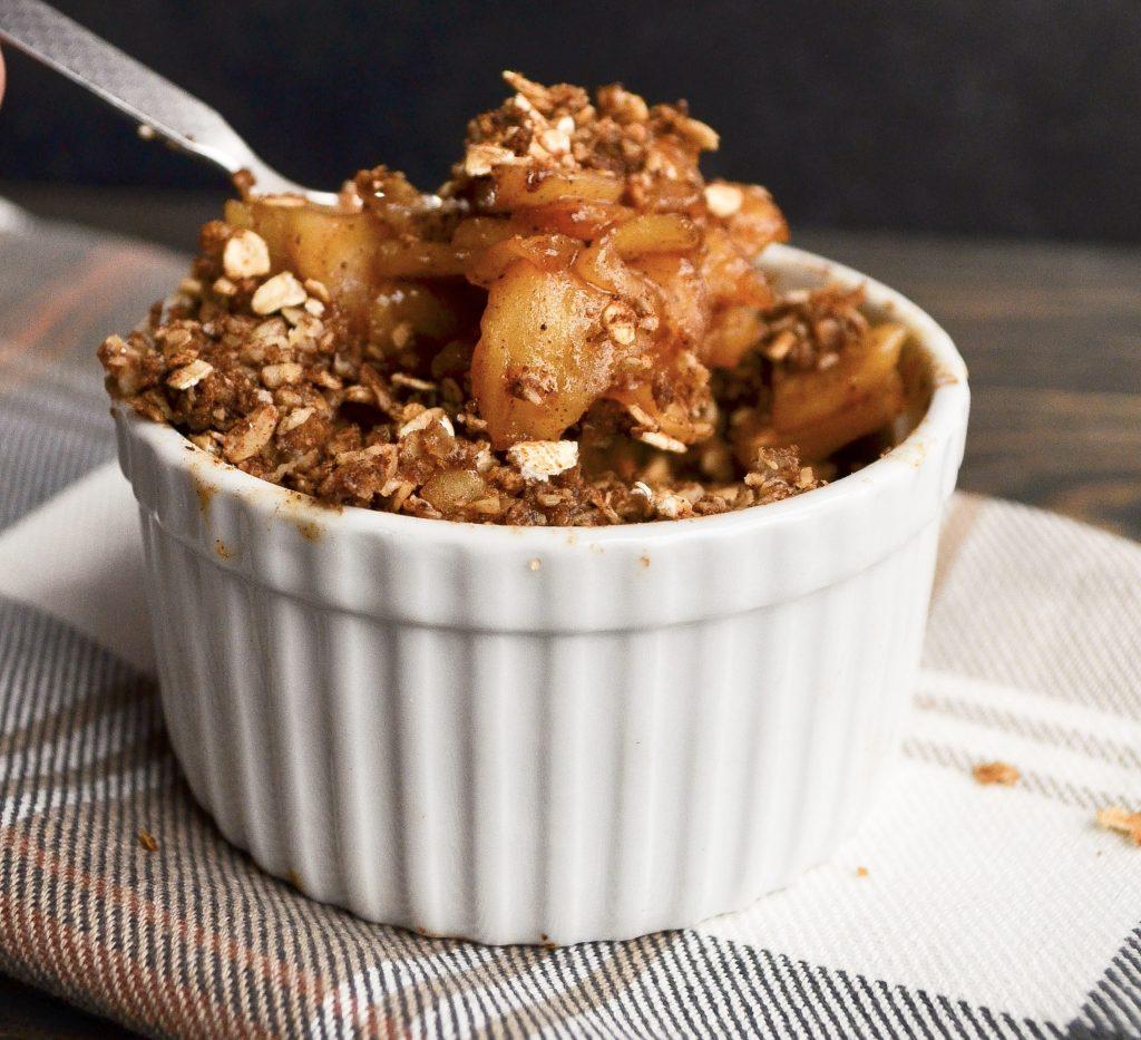 Overhead shot of a single-serving apple crisp in a ramekin, with a spoon beside it, ready to be eaten