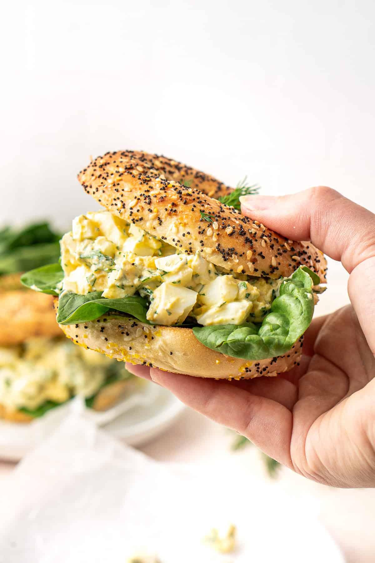 A person enjoying a bagel with egg salad and lettuce outdoors