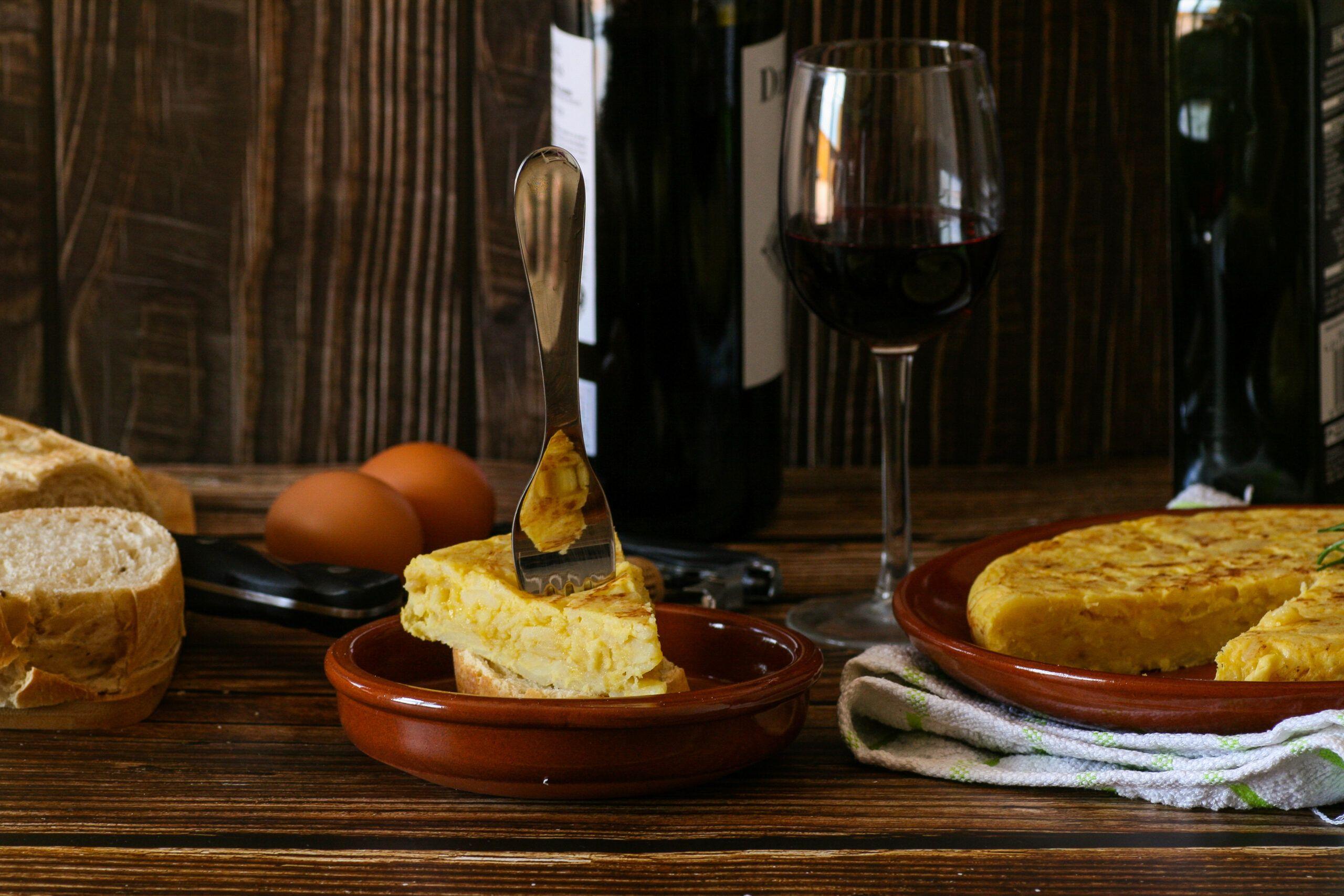A rustic wooden table with a golden brown Tortilla Española, garnished with fresh parsley, and a glass of Rioja wine.