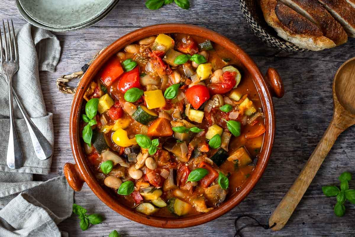 A rustic bowl of hearty Mediterranean vegetable stew, garnished with fresh herbs and a drizzle of olive oil.