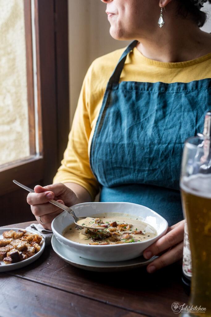 A person happily serving a steaming bowl of soup, with a side of crusty bread.
