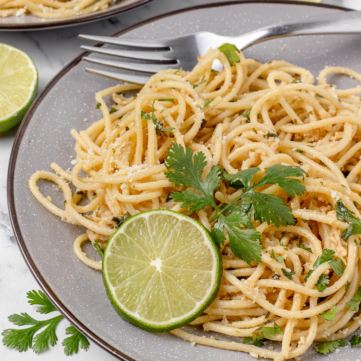 A wider shot of the pasta dish, showing a full serving, garnished with fresh cilantro and lime wedges.