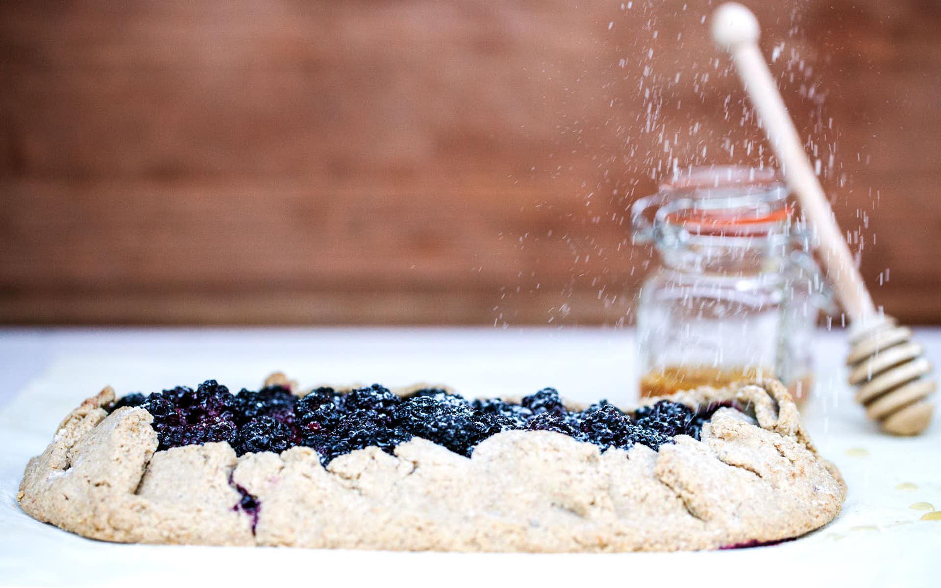 A rustic blackberry thyme tart on a white linen tablecloth with fresh blackberries and thyme sprigs scattered around
