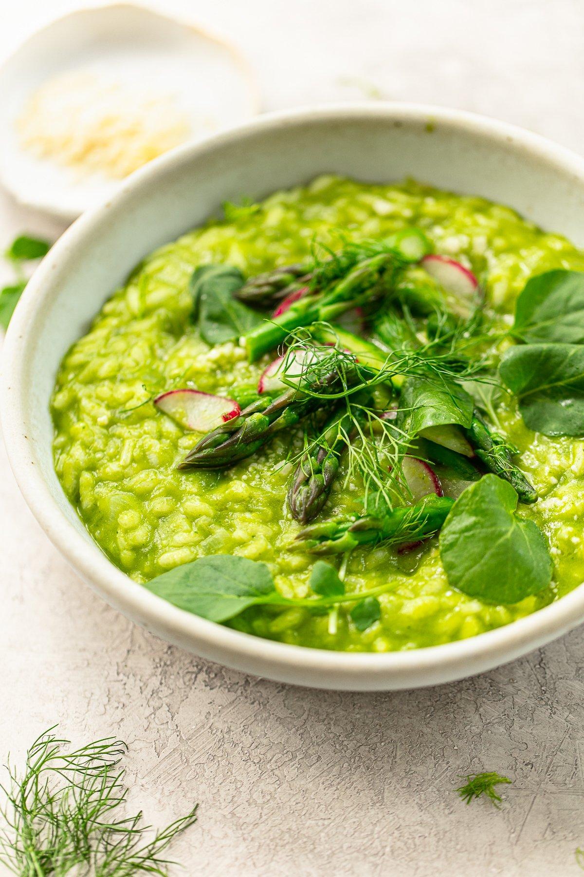 A vibrant, creamy risotto with bright green asparagus spears and thin slices of radish, garnished with fresh dill