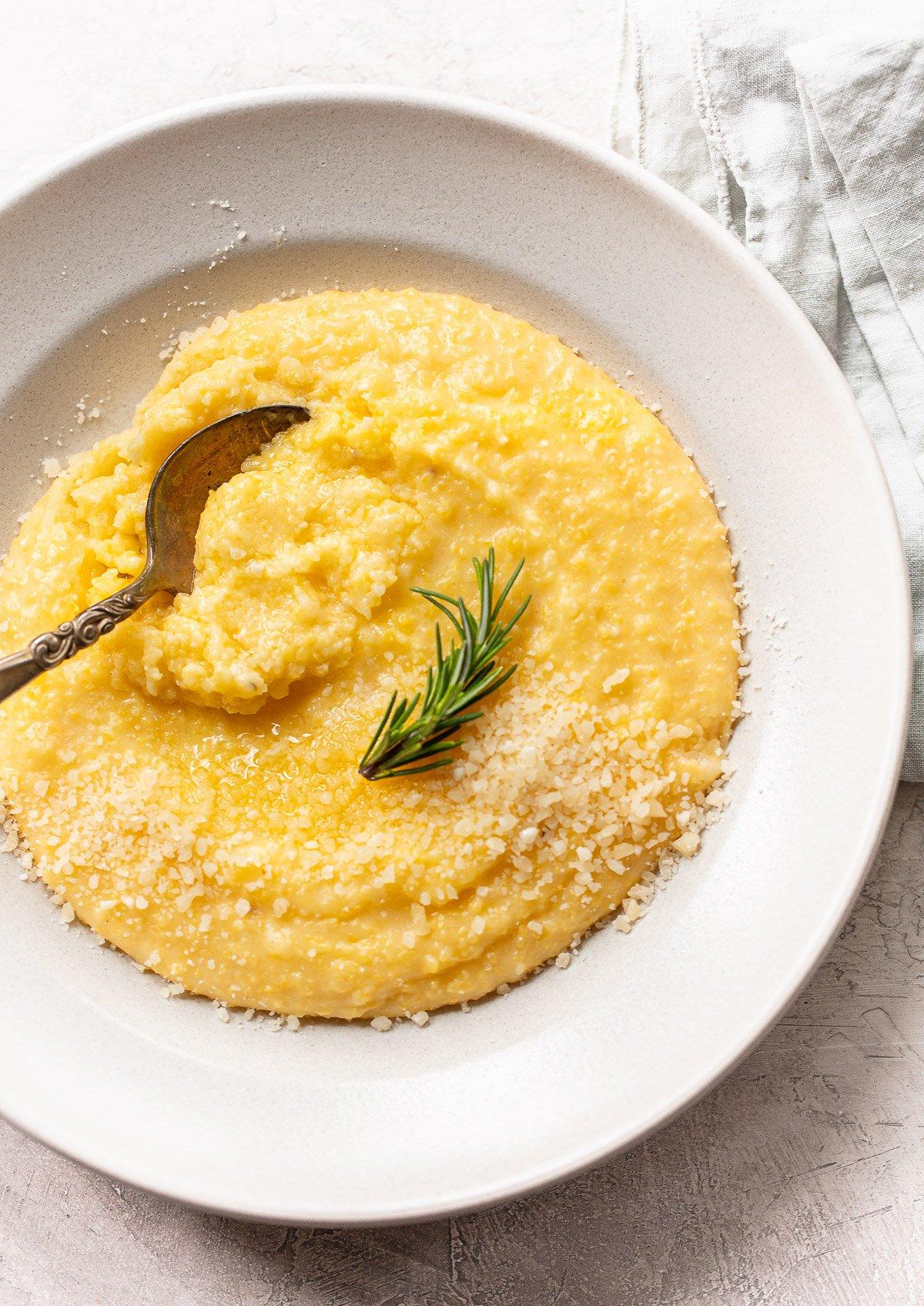 A rustic wooden table set with a plate of polenta cakes, a bowl of sautéed kale, and a sprinkle of parmesan cheese