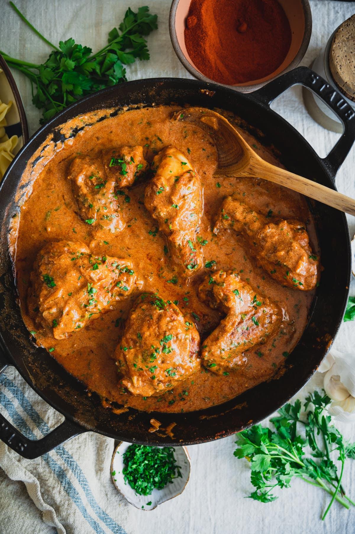 A rustic wooden table set for dinner with a bowl of chicken paprikash in the center