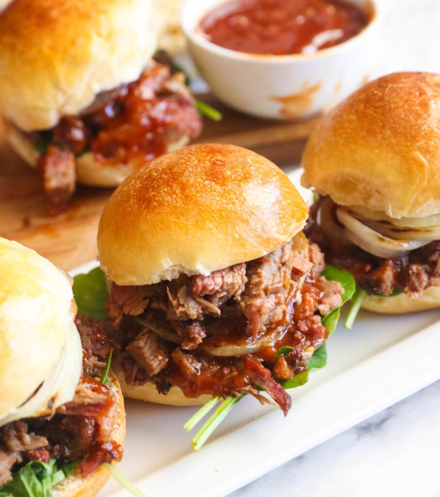 Close-up shot of delicious smoked brisket sliders with thousand island dressing on a rustic wooden board