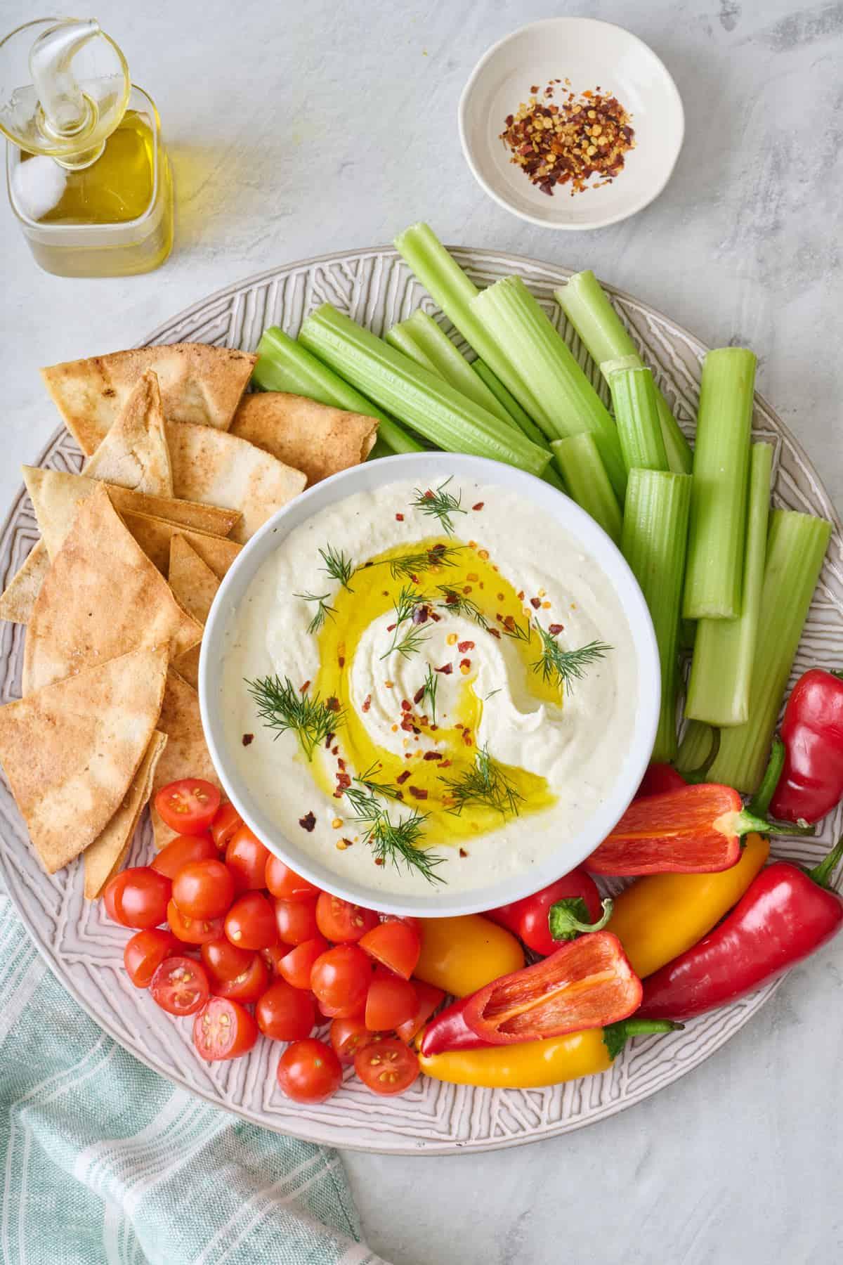 A bowl of creamy feta dip with pita bread and crudités arranged artfully around it.