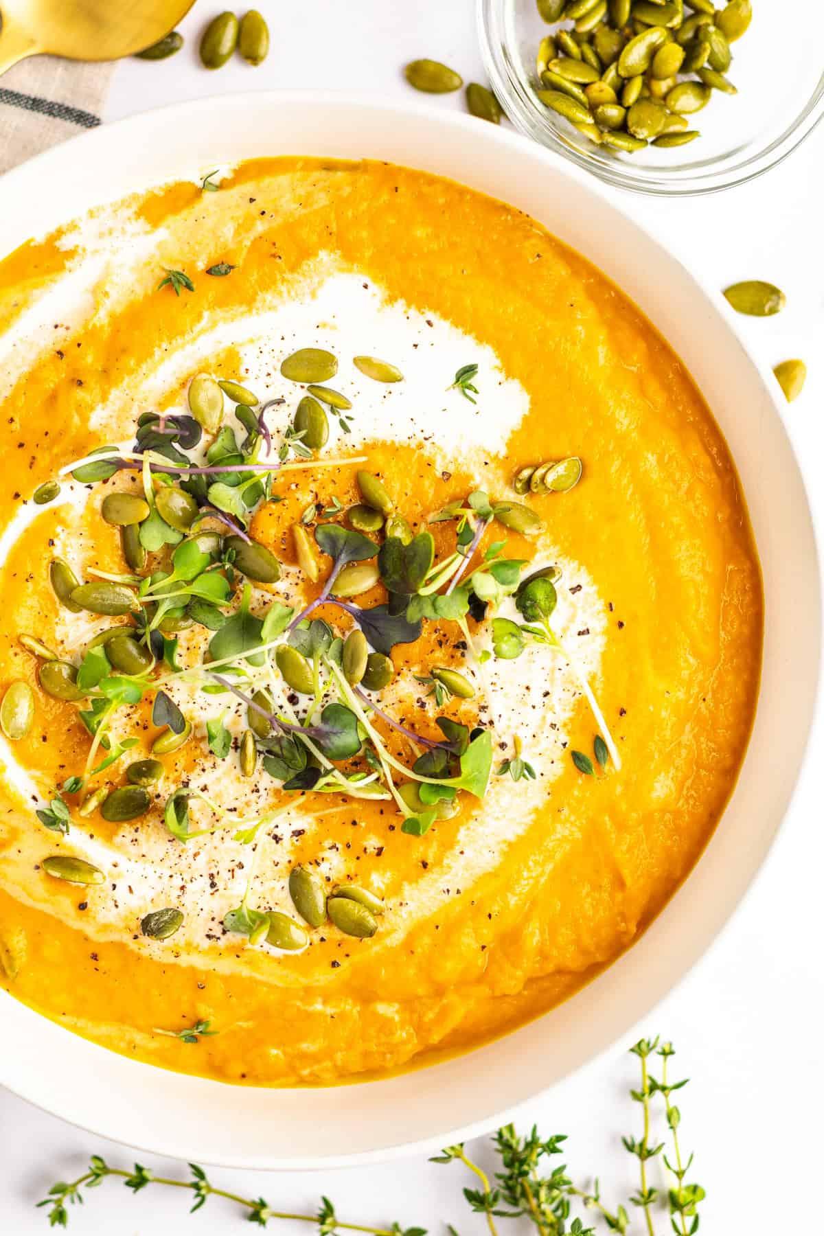 A rustic bowl of creamy pumpkin soup with a side of rice, garnished with pepitas