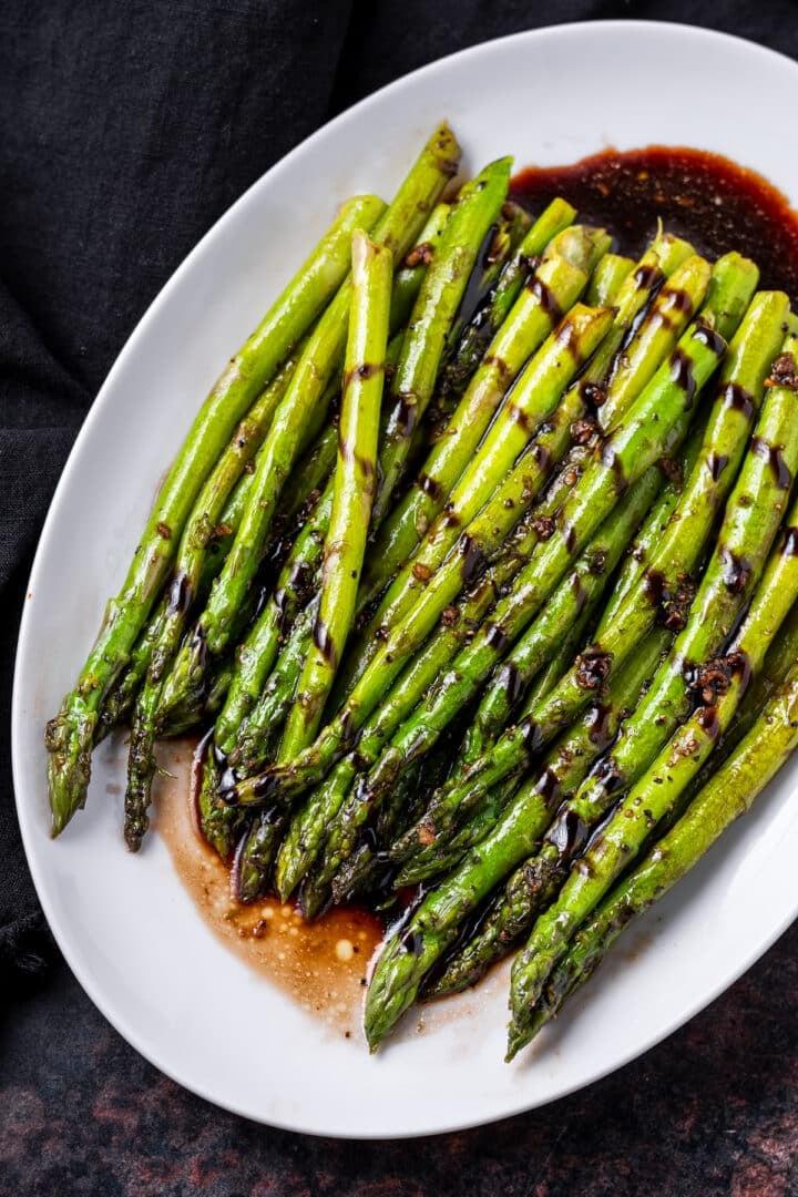 Close-up shot of sautéed asparagus with a glossy balsamic reduction, garnished with fresh herbs