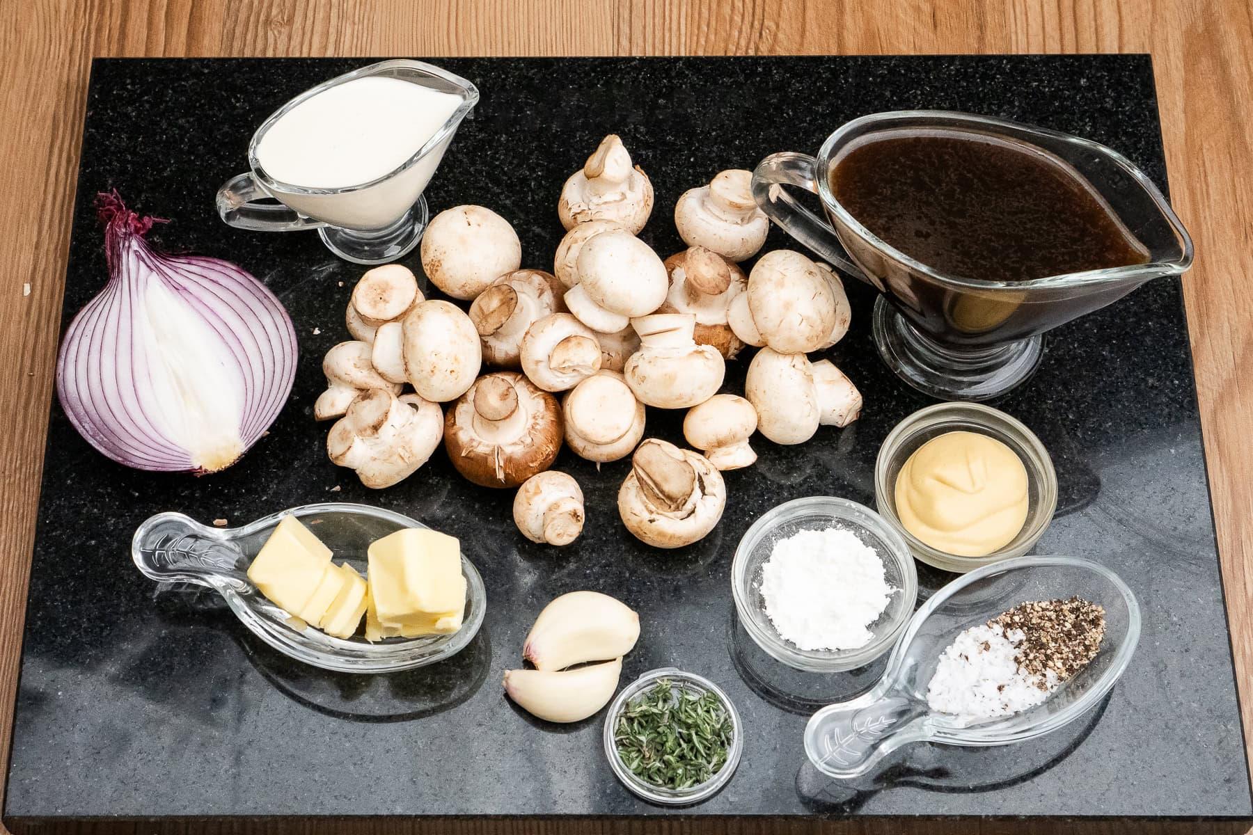 Ingredients for homemade mushroom sauce: sliced mushrooms, garlic, onion, cream, broth on a cutting board