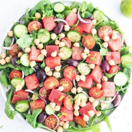 a vibrant and refreshing watermelon and chickpea salad served in a white bowl on a picnic blanket