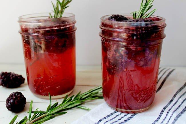 Close-up of a jar of blackberry rosemary syrup with fresh blackberries and rosemary sprigs