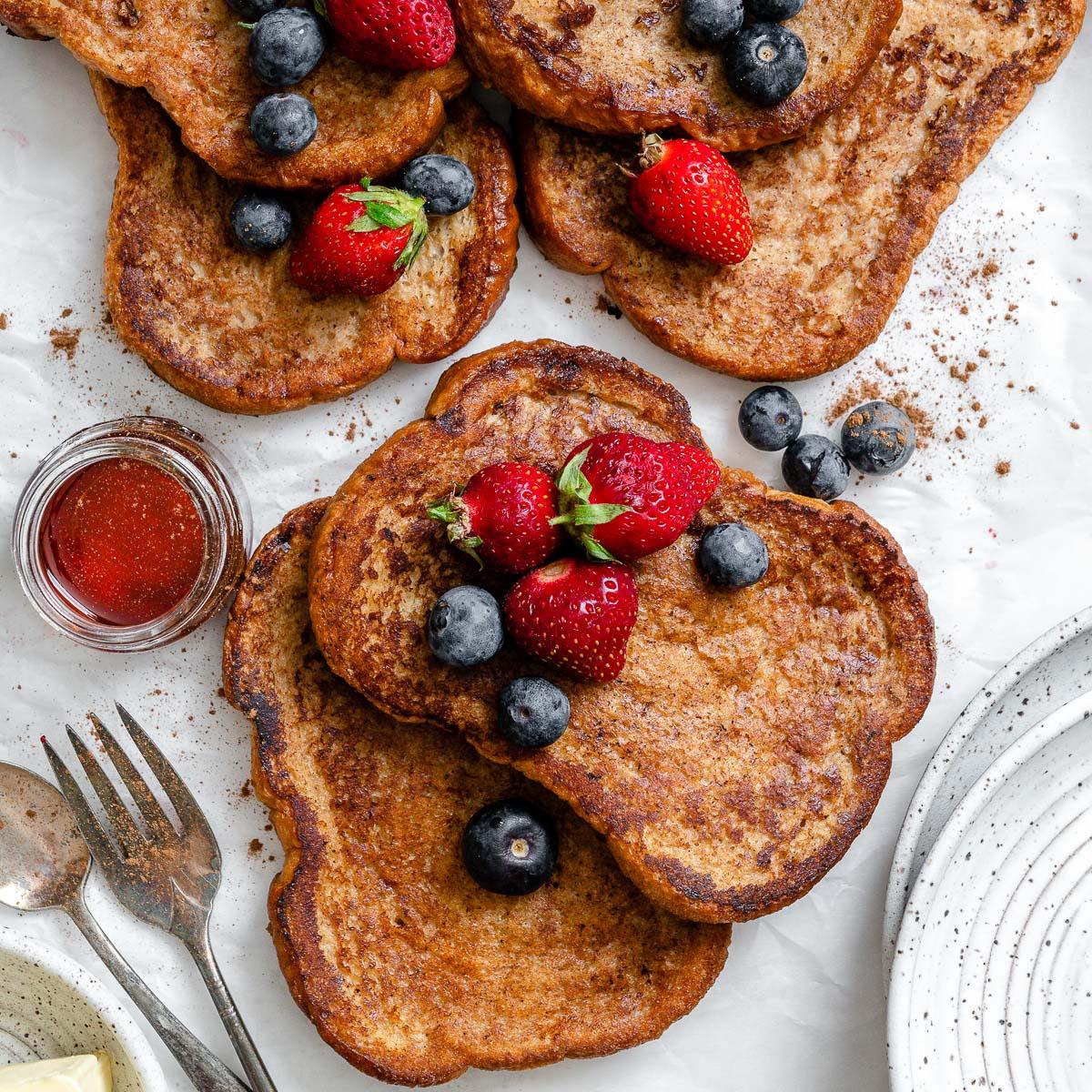 Golden-brown slices of vegan French toast on a plate, garnished with fresh berries and a dusting of powdered sugar.