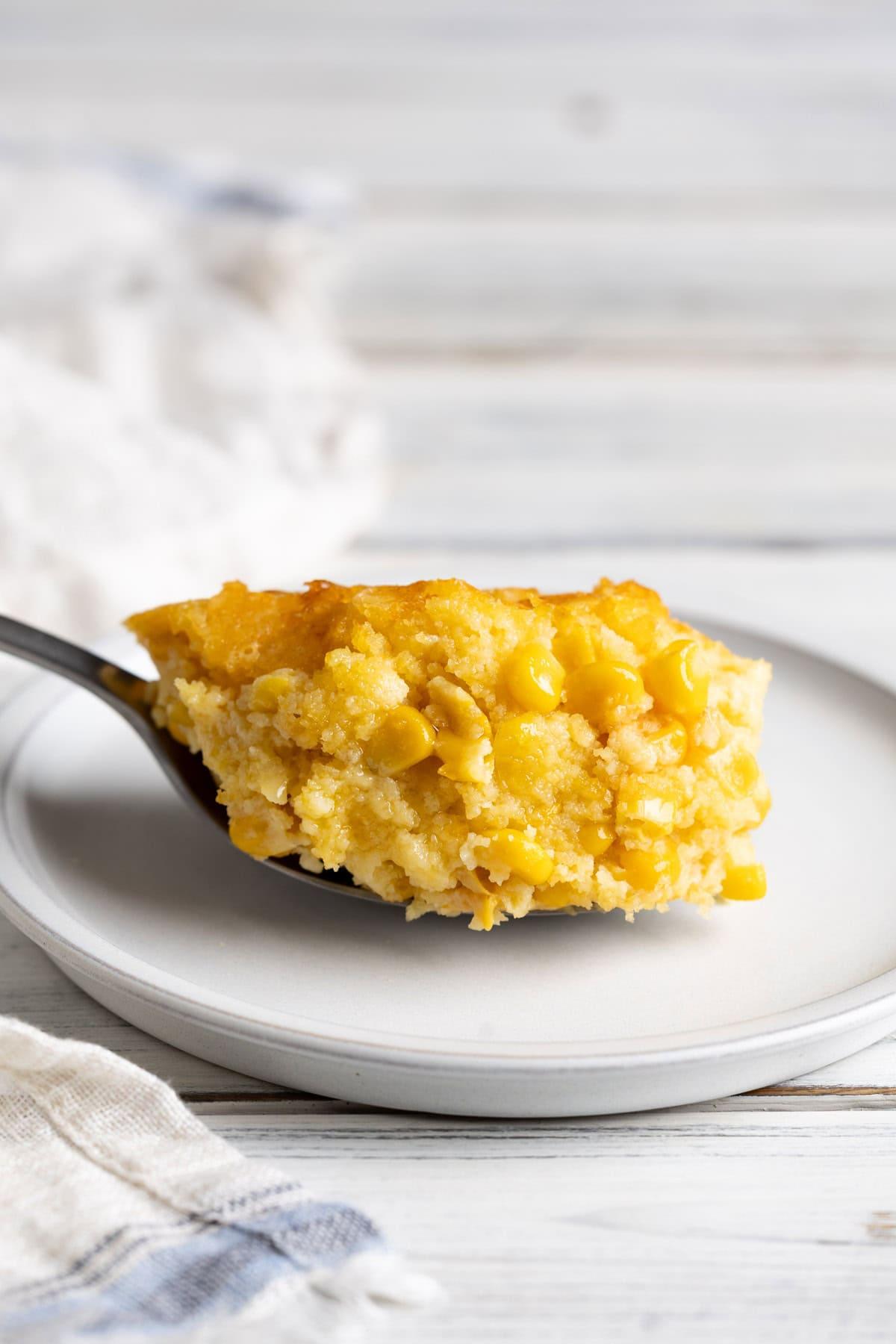 Scoop of creamy baked corn casserole on a plate next to a serving spoon