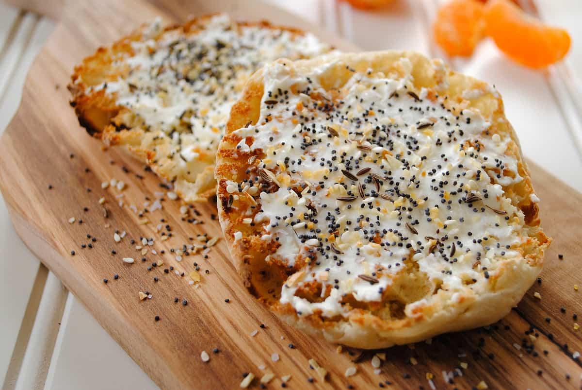 Close-up shot of a muffin being broken apart to show the soft inside, with everything bagel seasoning sprinkled on top