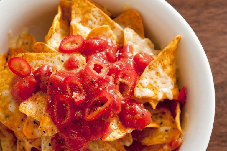 Close-up of a single nacho chip with pomegranate sauce dripping down