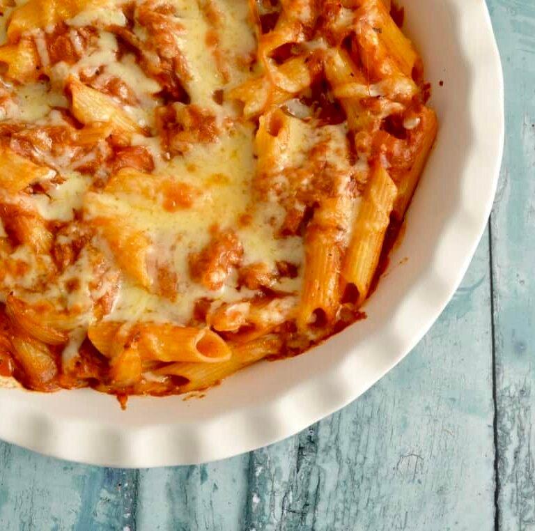 A rustic bowl of gluten-free pasta with tender pulled pork, garnished with fresh herbs and a drizzle of sauce