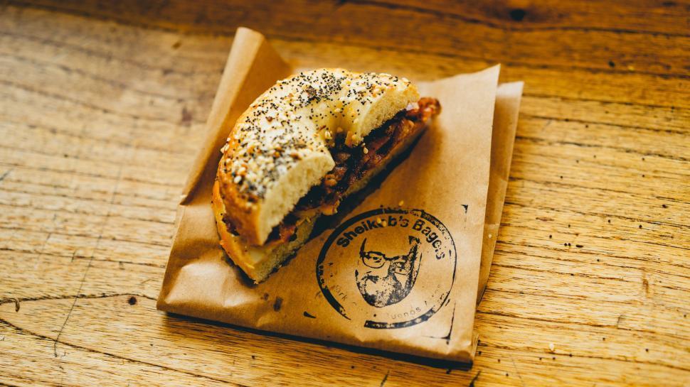 A rustic wooden table with a plate of golden-brown Everything Bagel Muffins, some with a slightly crispy top, surrounded by fresh chives
