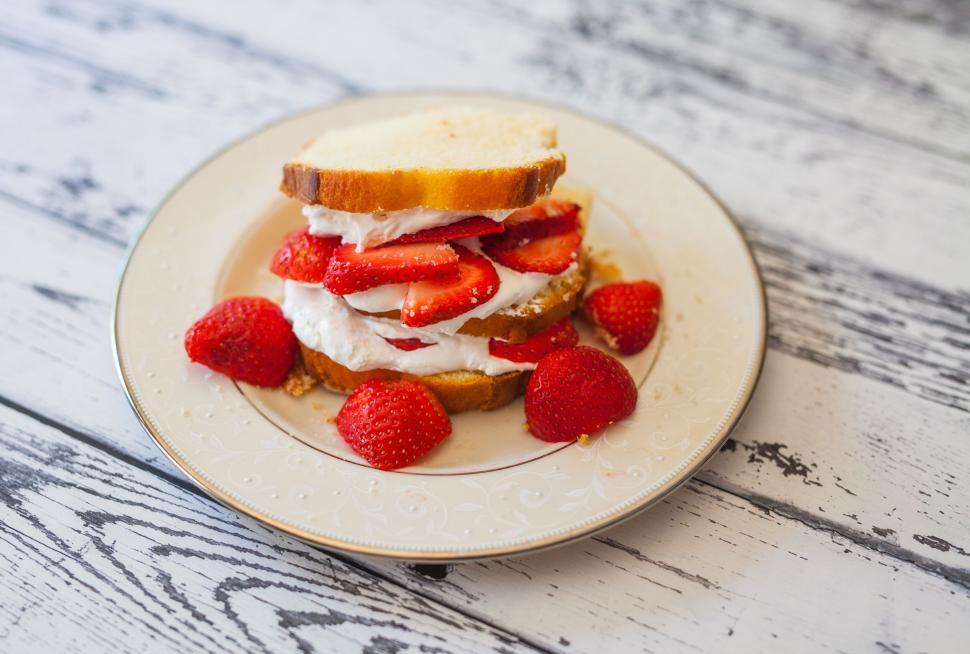 A rustic wooden table with a plate of strawberry shortcakes, fresh strawberries, and a pitcher of cream