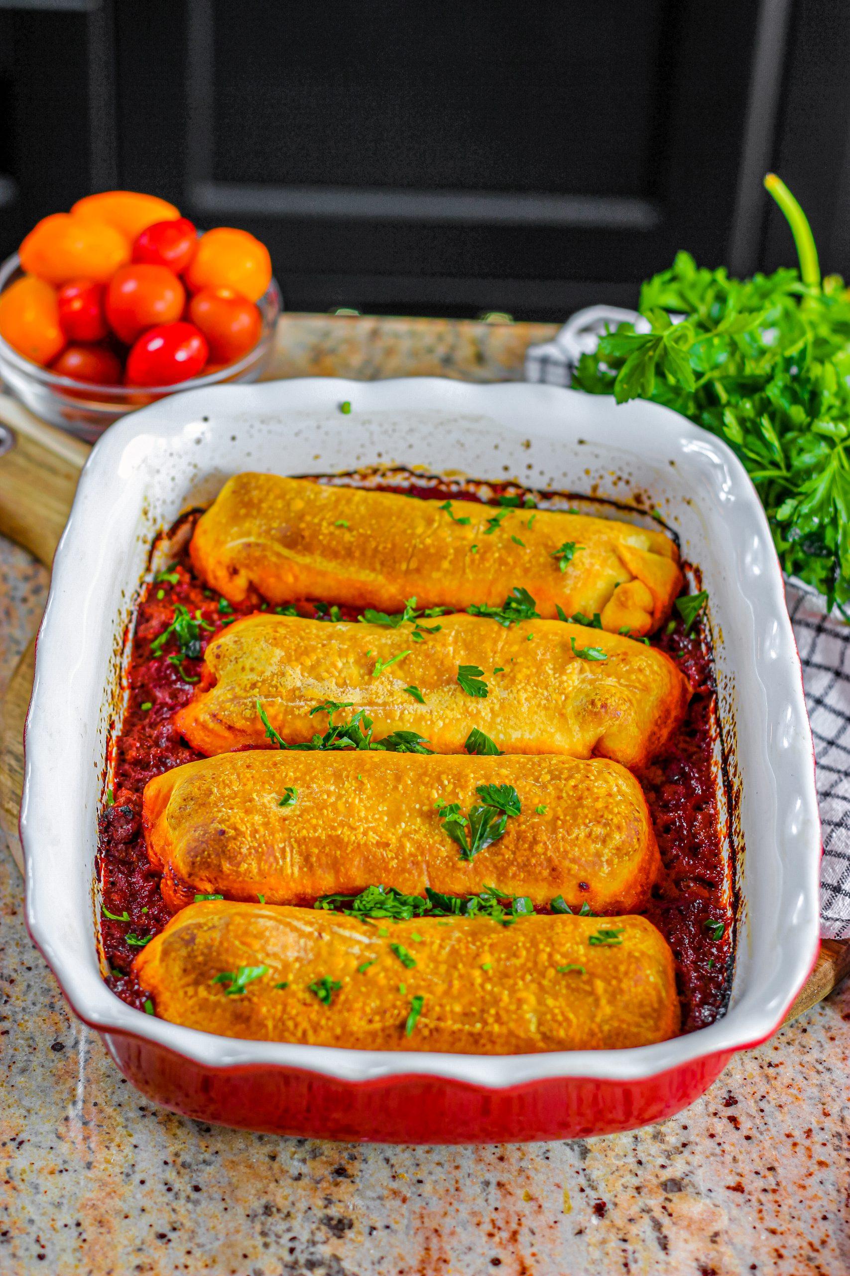 A baking dish filled with golden brown, cheesy hot dog enchiladas.