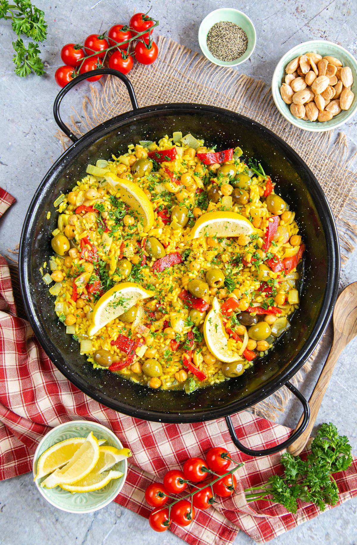 A vibrant red lentil and vegetable paella in a large pan, garnished with fresh parsley