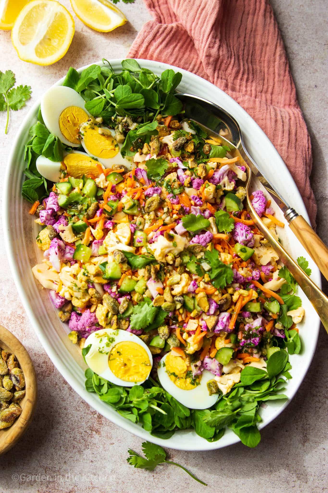 A vibrant and colorful bowl of cauliflower rice salad with chickpeas and feta, garnished with fresh herbs.